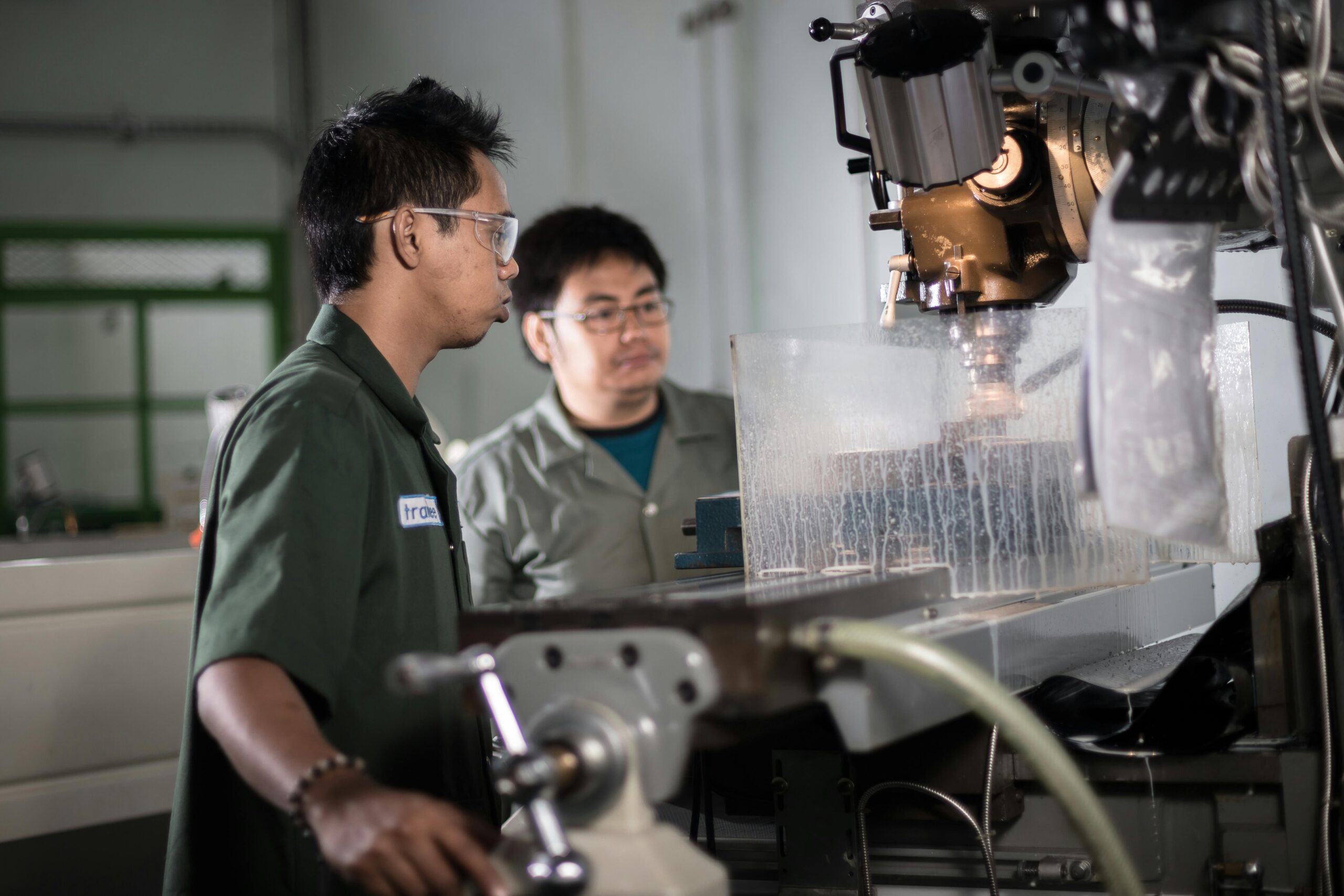 Two technicians in a workshop in Indonesia operating a CNC machine, focused on precision engineering.